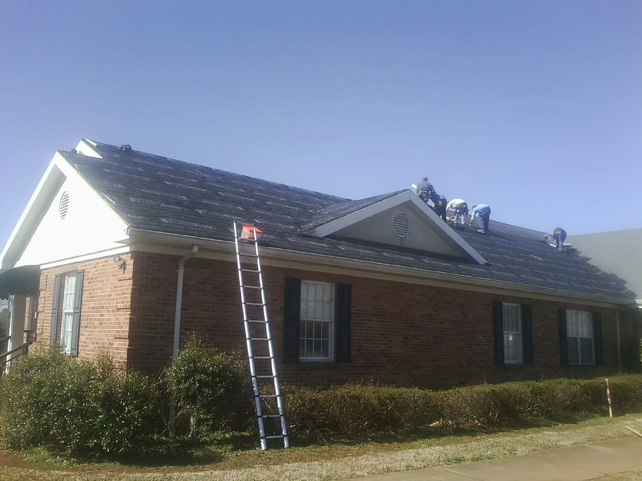 Crew tearing shingles off a brick ranch roof with a ladder set — Emergency Roof Repair work by our crew in Kinzers