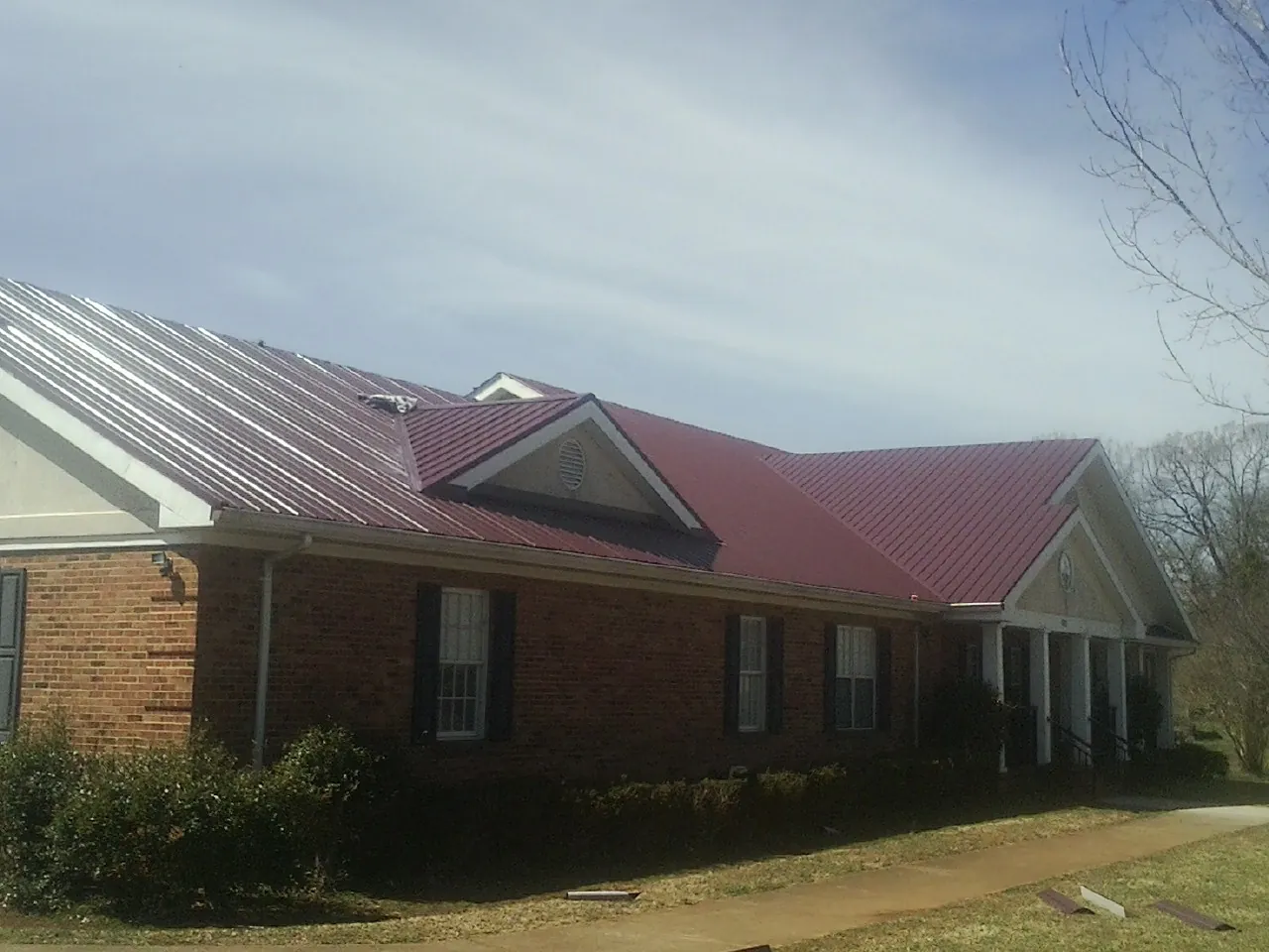 Red metal roof with gabled entries on a long brick building, from a Hail Damage Roof Repair job in Kinzers