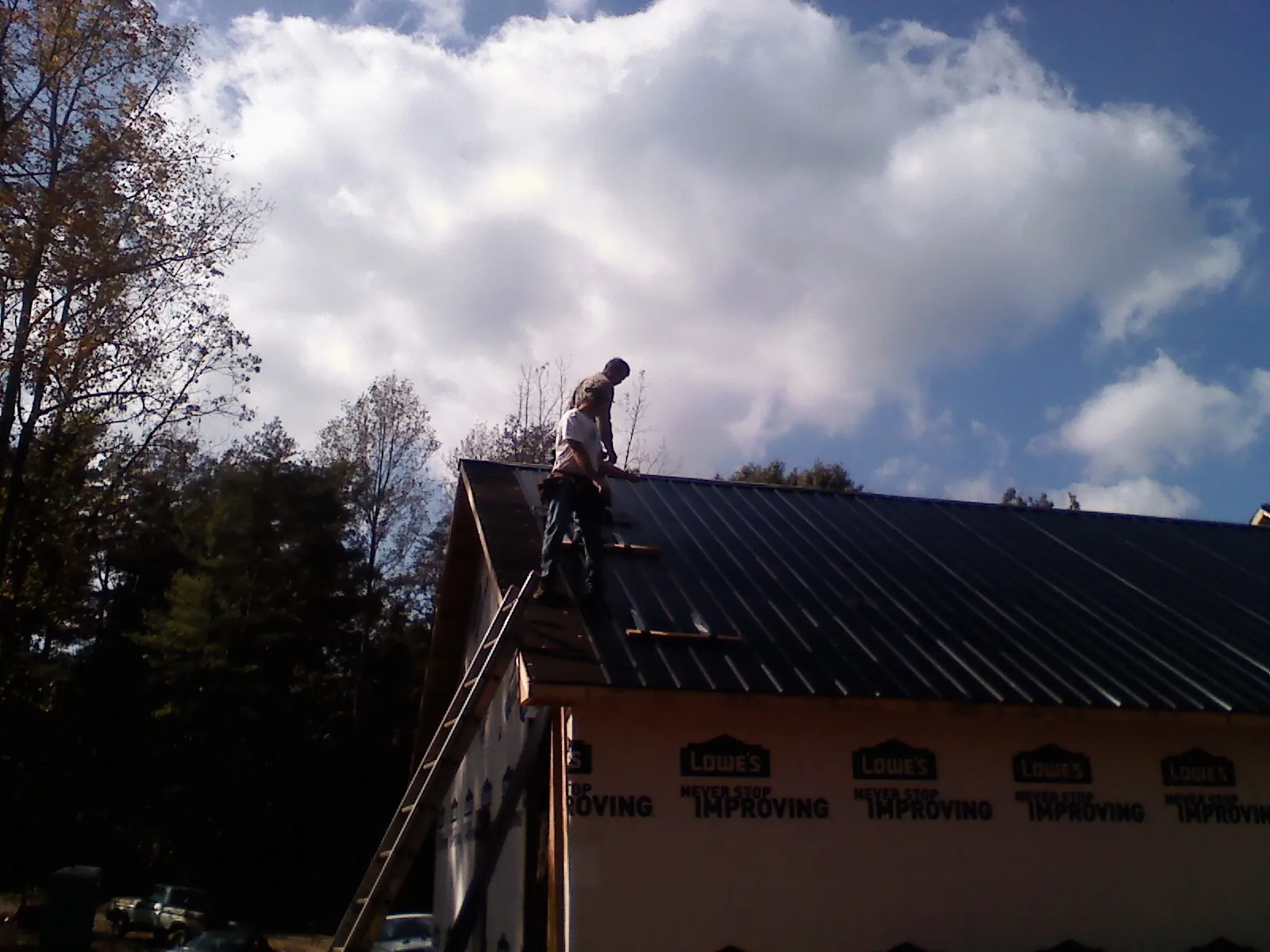 Roofer fastening dark metal panels high against a cloudy sky, from a Roof Inspection job in Kinzers