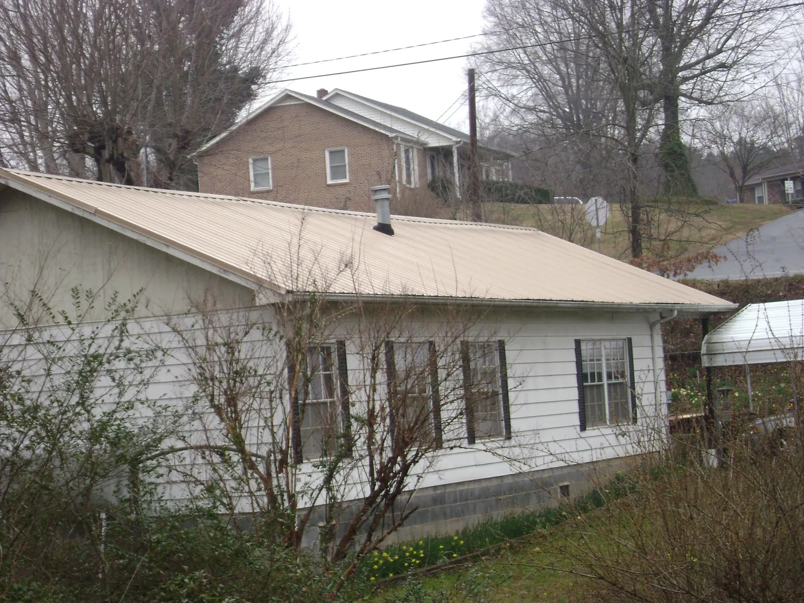Tan metal roof on a white sided house set into a hillside — Commercial Roofing by Roofing Brothers in Kinzers